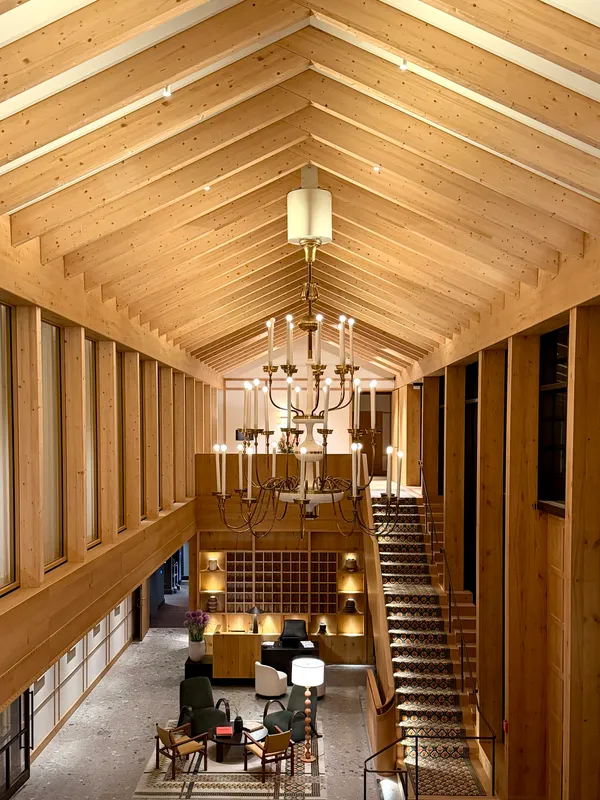 A tall timber lobby with a pitched wooden ceiling, a chandelier and a staircase.