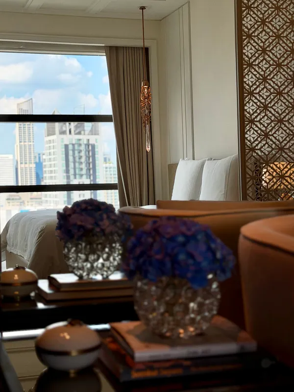 Blue hydrangeas on a side table in a hotel room, with tall windows onto the city.